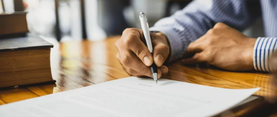 man in long sleeve shirt at desk signing document with pen