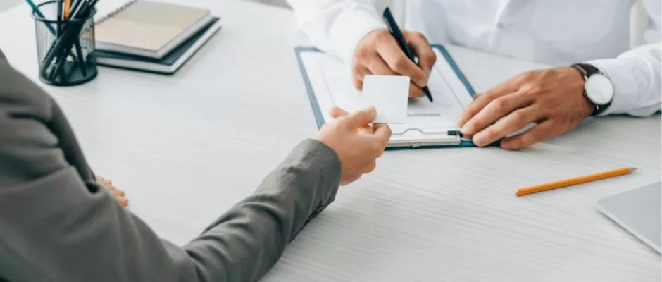 person handing doctor card as the doctor takes notes on keyboard